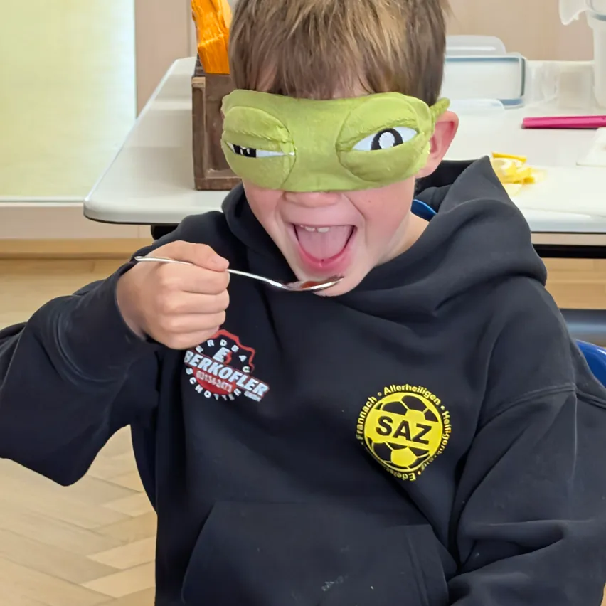 Ein junger Junge mit einem grünen Blindfold isst etwas mit einem Löffel.