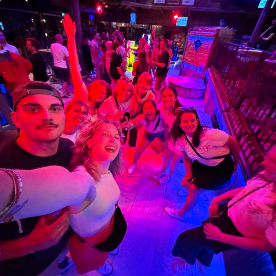 Eine Gruppe von Menschen lächelt und posiert für ein Foto in einem Club mit roten und lila Lichtern.