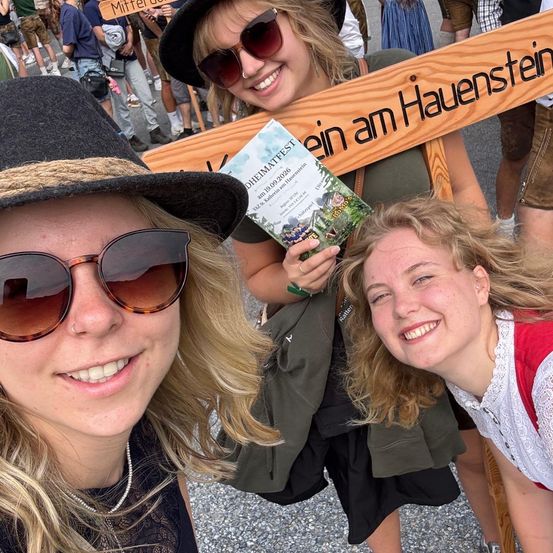 Drei Frauen lächeln auf einem Festival, eine hält ein Schild mit der Aufschrift 'ein am Hauenstein'.
