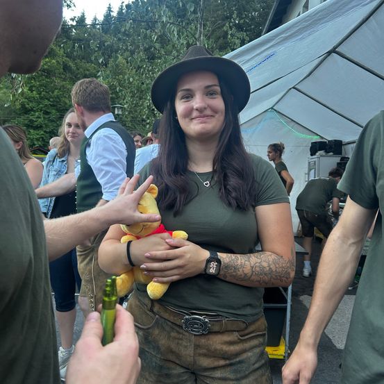 Eine Frau in einem grünen Shirt und Hut hält einen Winnie-the-Pooh-Plüschtier in einer Menschenmenge bei einer Veranstaltung im Freien.