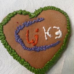 Ein herzförmiger Lebkuchen mit grüner Glasur am Rand und weißer Glasur, die die Buchstaben 'W' und 'K' im Inneren bildet.