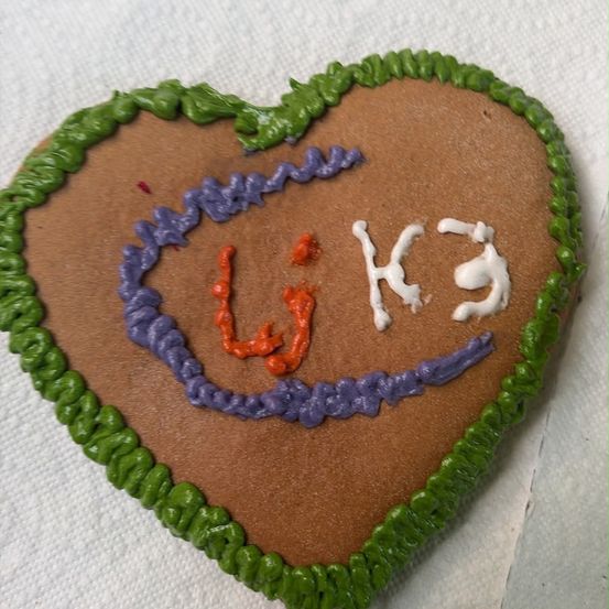 Ein herzförmiger Lebkuchen mit grüner Glasur am Rand und weißer Glasur, die die Buchstaben 'W' und 'K' im Inneren bildet.
