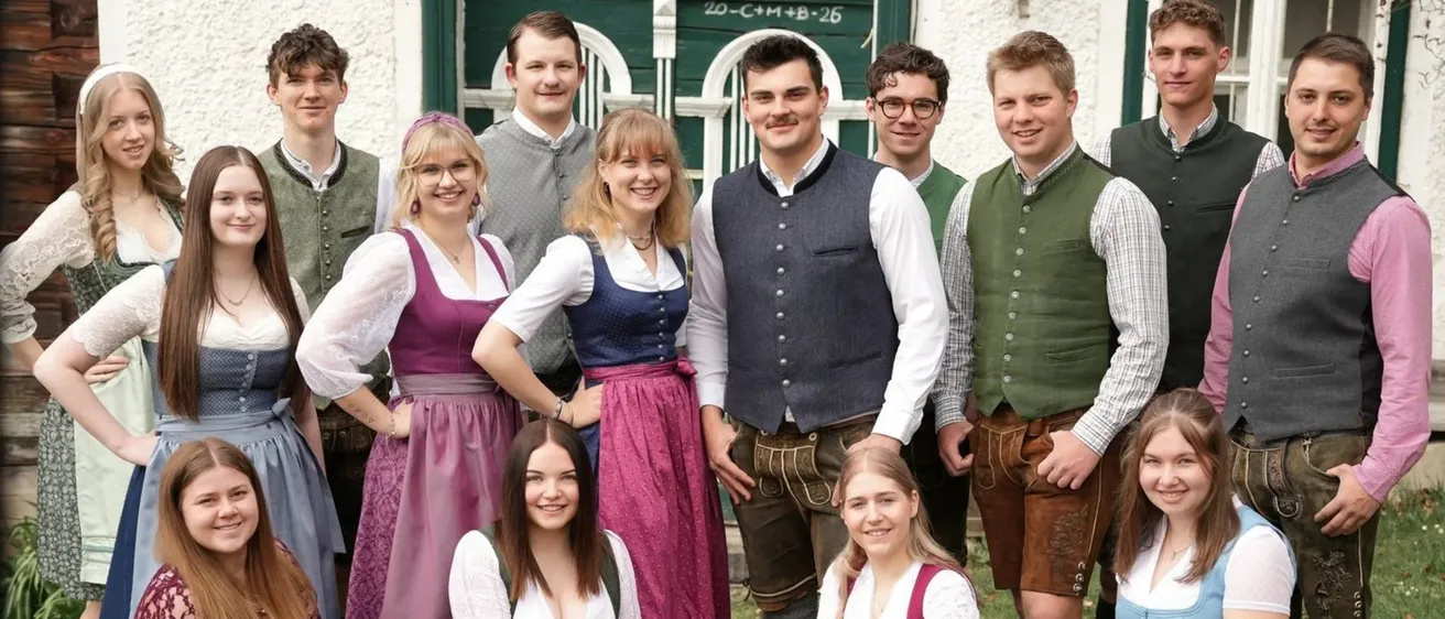 Eine Gruppe von Menschen in traditioneller bayerischer Kleidung posiert für ein Foto vor einem Gebäude.