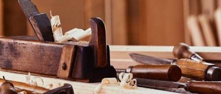 Ein Holzarbeitstisch beherbergt verschiedene Werkzeuge, darunter ein Meißel, eine Hobel und ein Messer. Die Werkzeuge sind von Holzspänen umgeben.