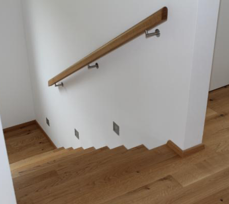 Innenansicht eines Hauses mit Holztreppe und einer weißen Wand mit einem Holzgeländer und Metallgriffen.