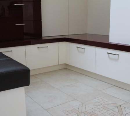 Eine moderne Küche mit weißen Schränken, einer dunklen Arbeitsplatte und einem schwarzen Ledersitz in der Ecke. Der Boden ist mit einem geometrischen Muster gefliest.