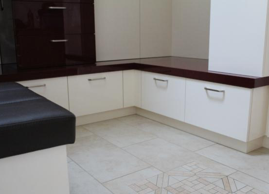 Eine moderne Küche mit weißen Schränken, einer dunklen Arbeitsplatte und einem schwarzen Ledersitz in der Ecke. Der Boden ist mit einem geometrischen Muster gefliest.