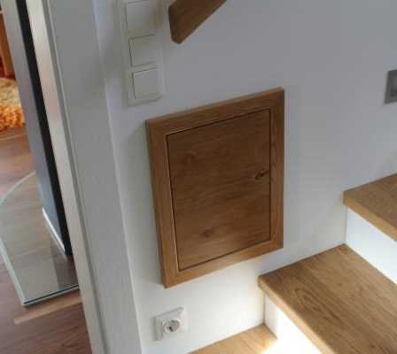 Eine Holztür ist an der Wand zwischen den Stufen montiert. Die Stufen sind aus Holz mit weißen Abschlüssen. Eine Steckdose und ein Schalter sind an der Wand montiert.