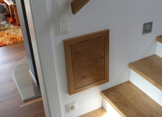Eine Holztür ist an der Wand zwischen den Stufen montiert. Die Stufen sind aus Holz mit weißen Abschlüssen. Eine Steckdose und ein Schalter sind an der Wand montiert.