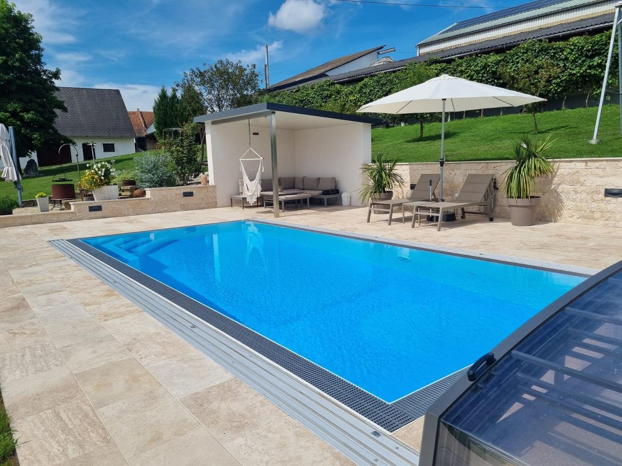 Ein Swimmingpool im Freien mit Terrasse, Liegestühlen und einem Sonnenschirm. Es gibt eine Hängematte und eine kleine Couch im Terrassenbereich.