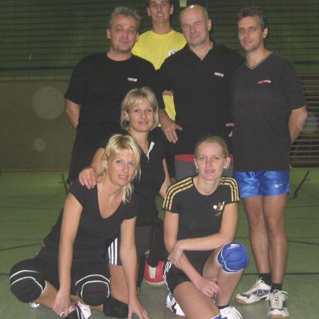 Eine Gruppe von Personen, die schwarze und gelbe Sportbekleidung tragen, posiert für ein Foto auf einem Hallensportplatz, wahrscheinlich für ein Sportteam.