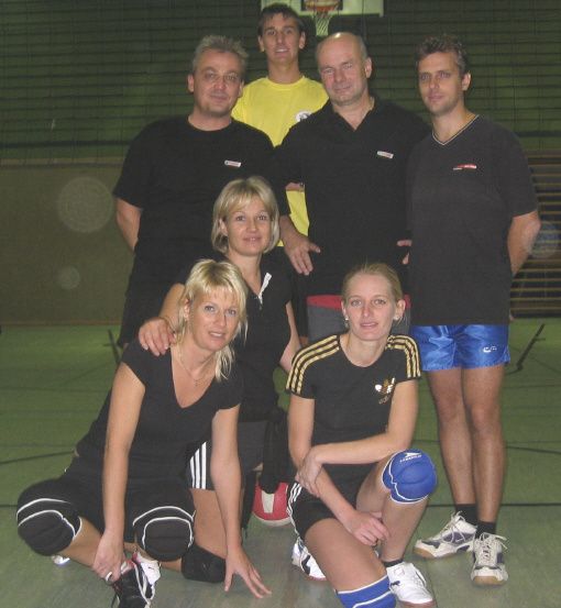 Eine Gruppe von Personen, die schwarze und gelbe Sportbekleidung tragen, posiert für ein Foto auf einem Hallensportplatz, wahrscheinlich für ein Sportteam.