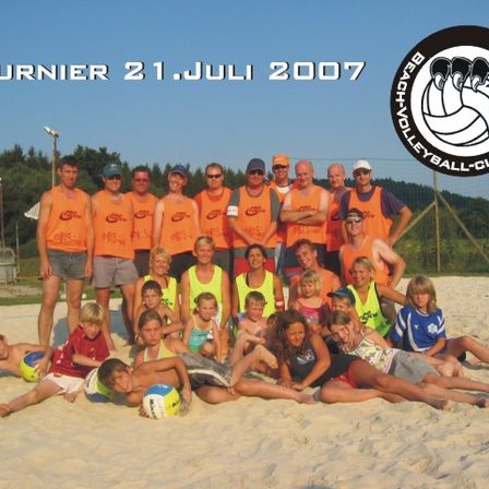 Gruppenfoto einer Volleyballmannschaft am Strand am 21. Juli 2007, mit Personen in orangen und gelben Westen und einem Volleyball in der Mitte.