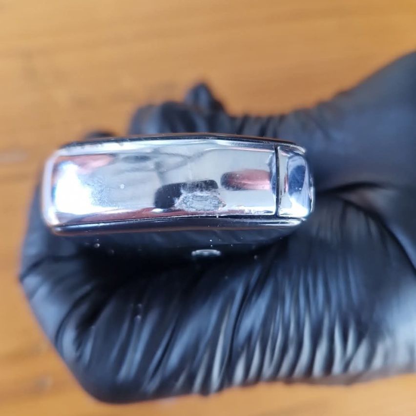 Eine Person, die schwarze Handschuhe trägt, hält ein glänzendes, metallisches Objekt in der Hand und reflektiert einen verschwommenen Hintergrund.