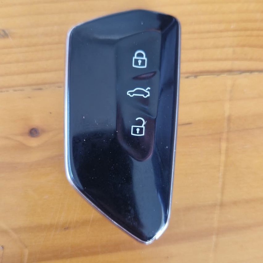 Ein schwarzer, glänzender Autoschlüssel mit drei Tasten, einschließlich Sperren, Entsperren und Auto, auf einer Holzoberfläche platziert.