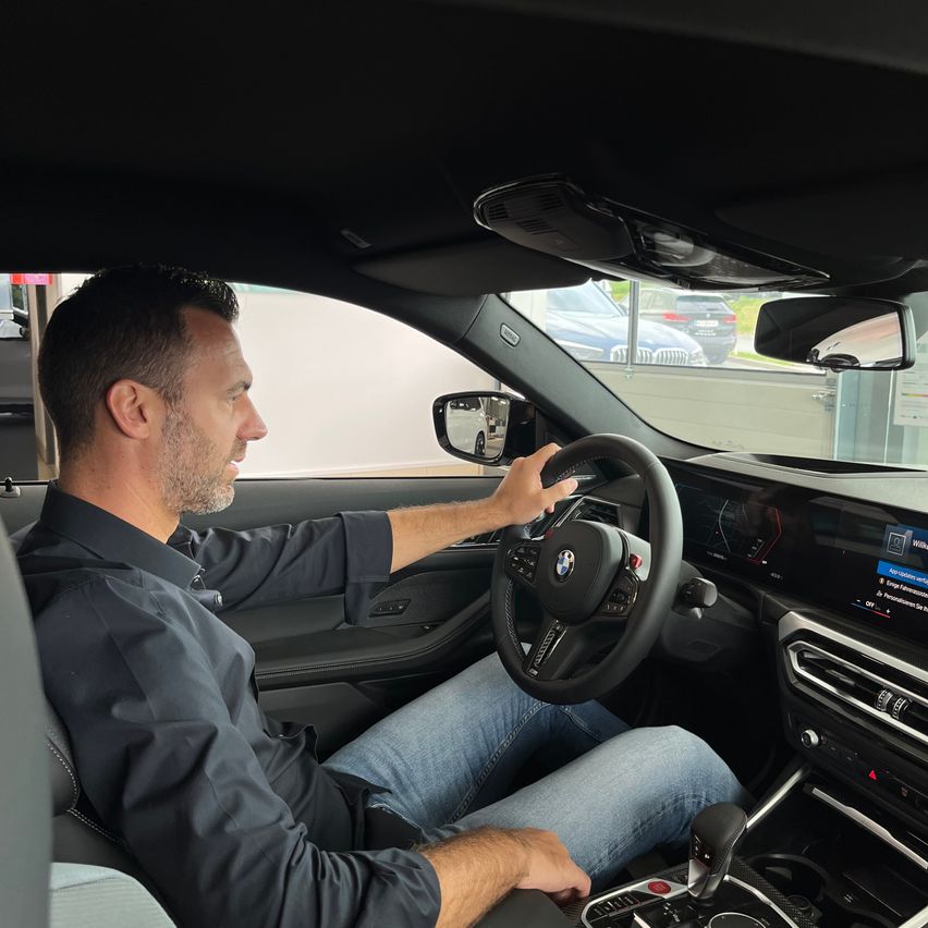 Ein Mann sitzt in einem BMW-Auto und hält das Lenkrad, mit einem modernen Armaturenbrett vor ihm.