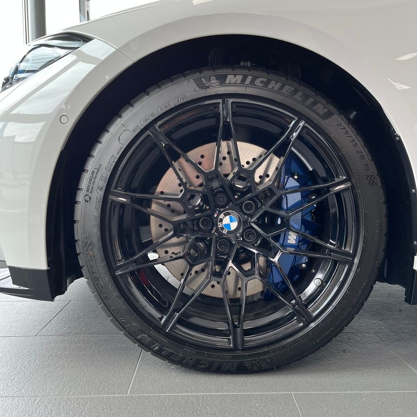 Ein weißer BMW-Wagen mit Michelin-Reifen, schwarzen Felgen und blauen Akzenten steht in einem Ausstellungsraum.