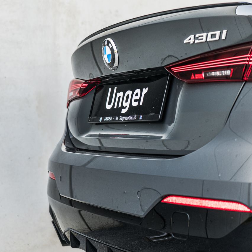 Die Heckseite eines dunkelgrauen BMW 430i ist zu sehen, mit einem Nummernschild mit dem Namen Unger. Das Auto hat rote Rücklichter.