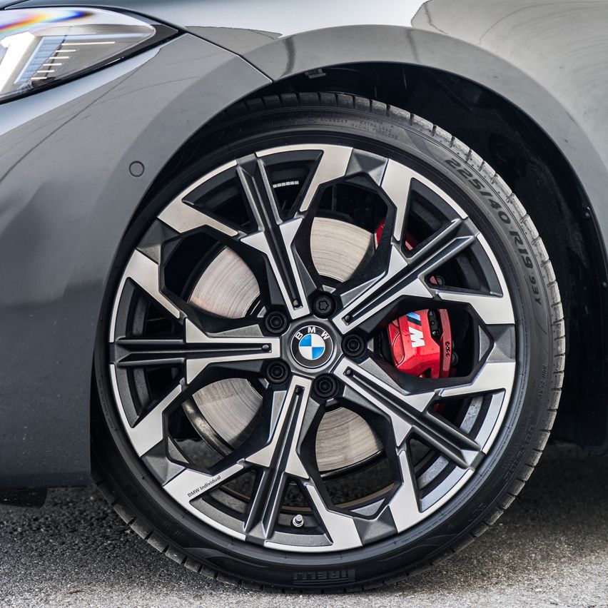 Eine Nahaufnahme eines BMW-Autorads mit silbernem Leichtmetallfelgen und roten Bremssätteln. Das Rad ist auf einem schwarzen Reifen mit weißen Buchstaben montiert.
