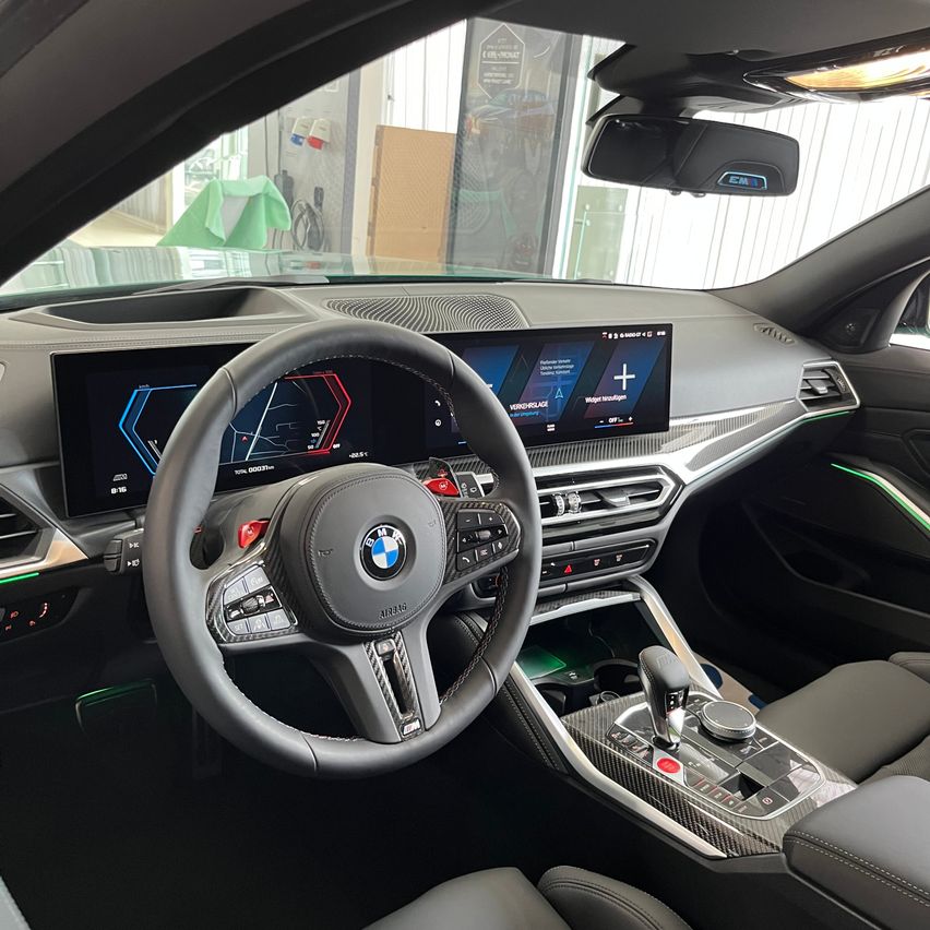 Innenraum eines BMW-Autos mit Lenkrad, Armaturenbrett und Bedienfeld. Das Armaturenbrett zeigt eine Navigationskarte.