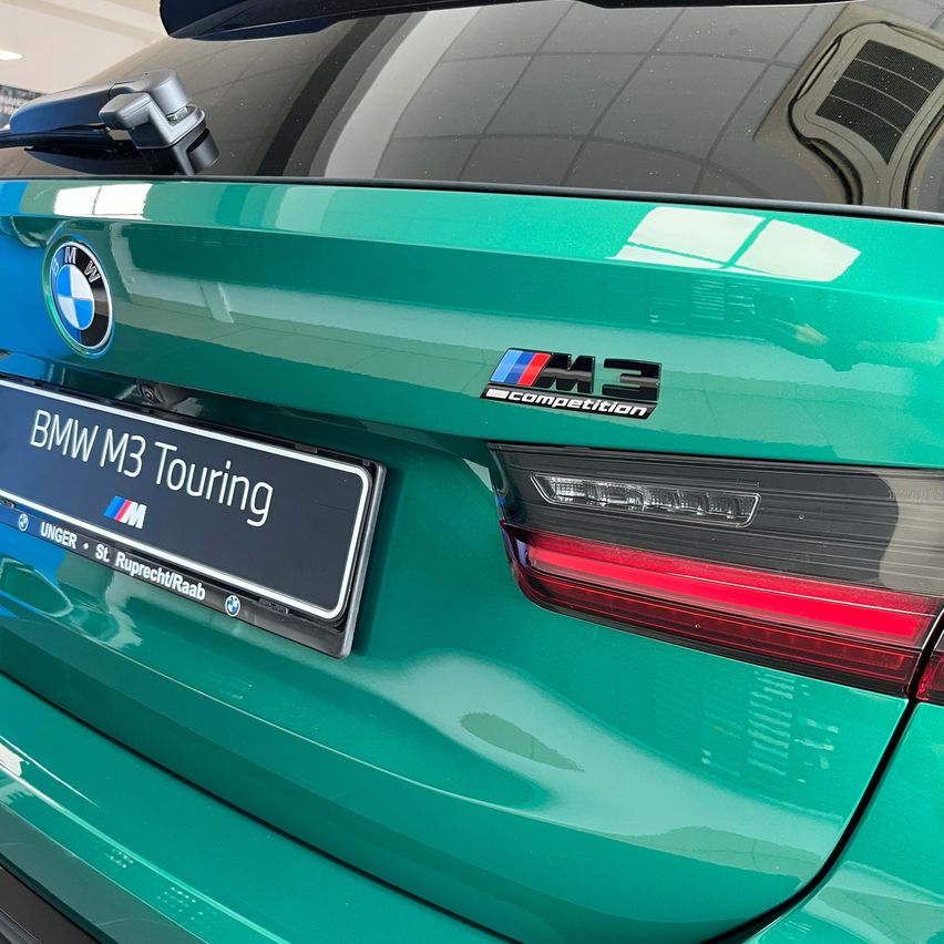 Die Heckansicht eines grünen BMW M3 Touring mit sichtbarem Nummernschild, BMW-Logo und rotem Rücklicht.