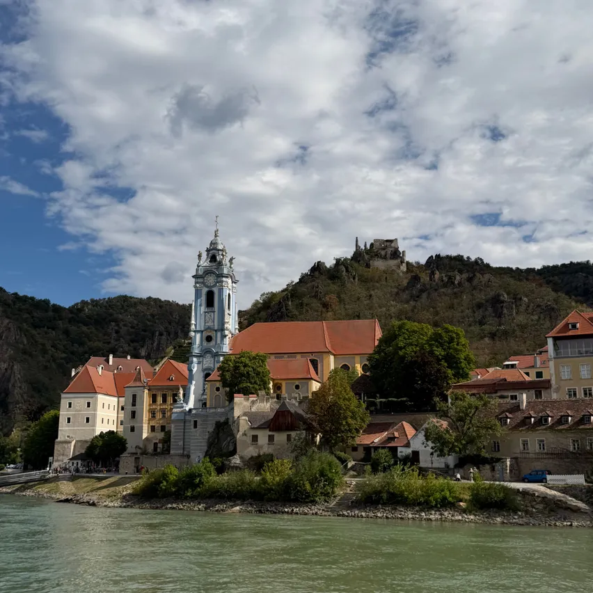 Eine malerische Ansicht einer historischen Stadt mit einem markanten Glockenturm, eingebettet zwischen einem Fluss und einem bergigen Hintergrund.