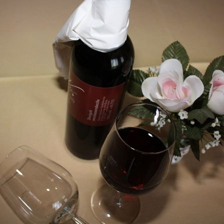 Eine Flasche Wein mit einer Serviette darauf steht neben einem Weinglas und zwei weißen Rosen in einem Vasen.