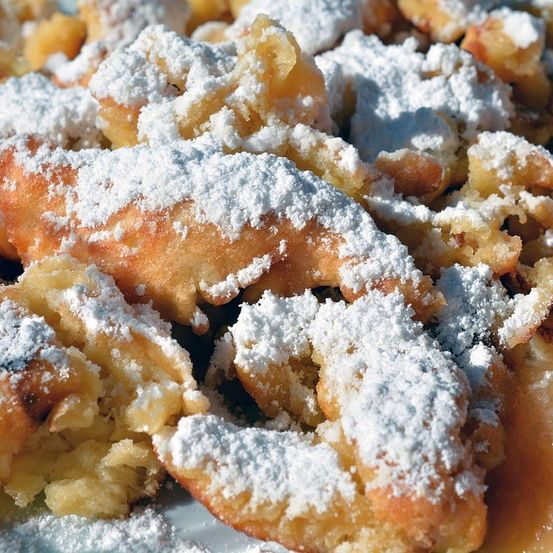 Nahaufnahme eines Tellers mit frittierten Teigstücken, bedeckt mit Puderzucker und Karamellsauce.