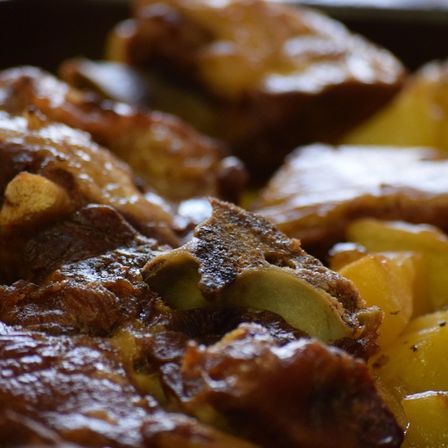 Eine Nahaufnahme von geschmortem Schweinebauch mit Kartoffeln. Das Fleisch ist glasig und knusprig, während die Kartoffeln zart sind.