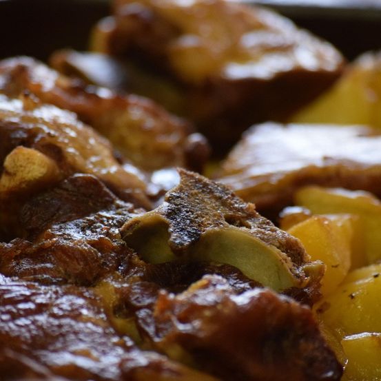 Eine Nahaufnahme von geschmortem Schweinebauch mit Kartoffeln. Das Fleisch ist glasig und knusprig, während die Kartoffeln zart sind.