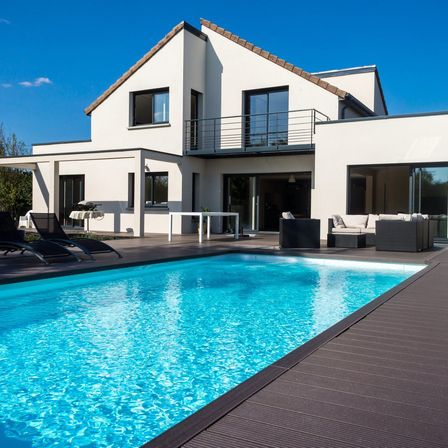 Ein modernes weißes Haus mit klarem blauem Himmel, mit Pool, Terrasse, Gartenmöbeln und Balkon mit Geländer.