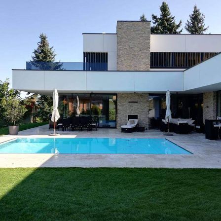 Modernes Haus mit Swimmingpool im Garten. Stühle und Tische sind für das Essen im Freien arrangiert. Bäume sind im Hintergrund.