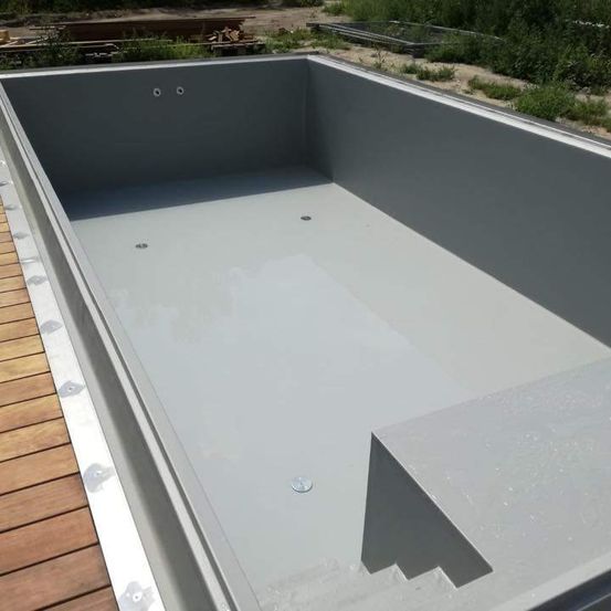 Ein leerer rechteckiger Pool mit einem Holzdeck. Der Pool besteht aus Beton und hat eine graue Auskleidung. Es gibt drei Löcher auf der Pooloberfläche.