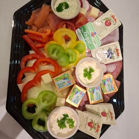 Ein schwarzer Teller mit einer Auswahl an Fleisch, Käse und Gemüse. Pfefferscheiben, Tomaten und verschiedene Dips sind auf dem Teller angeordnet.