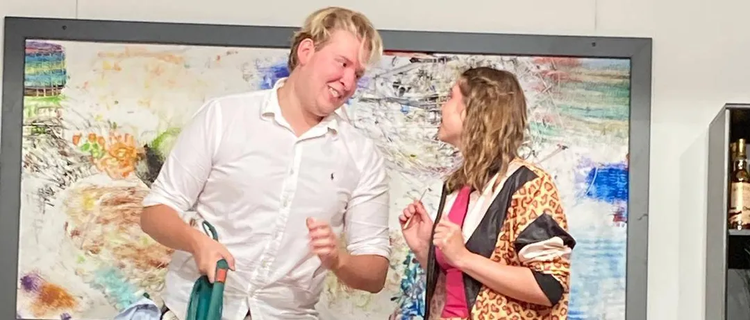 Ein Mann mit einem Staubsauger steht neben einer Frau in einem Leopardenmuster-Outfit, beide lächeln und sehen sich in einem Raum an.
