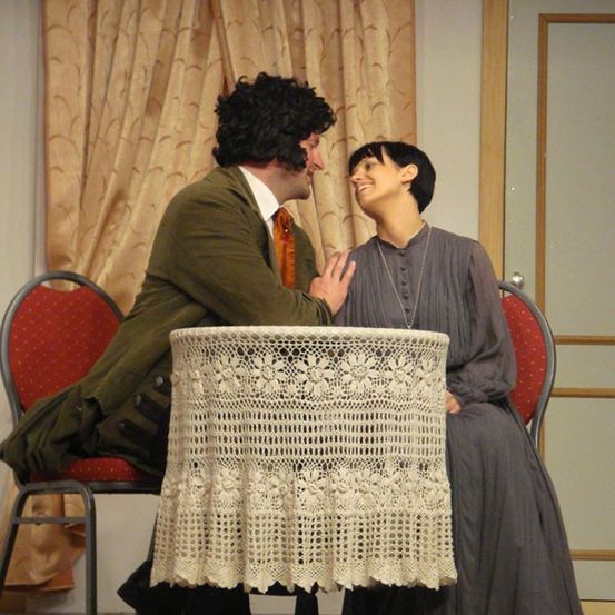 Ein Mann und eine Frau sitzen zusammen auf Stühlen vor einem Tisch, lächeln und schauen sich an.