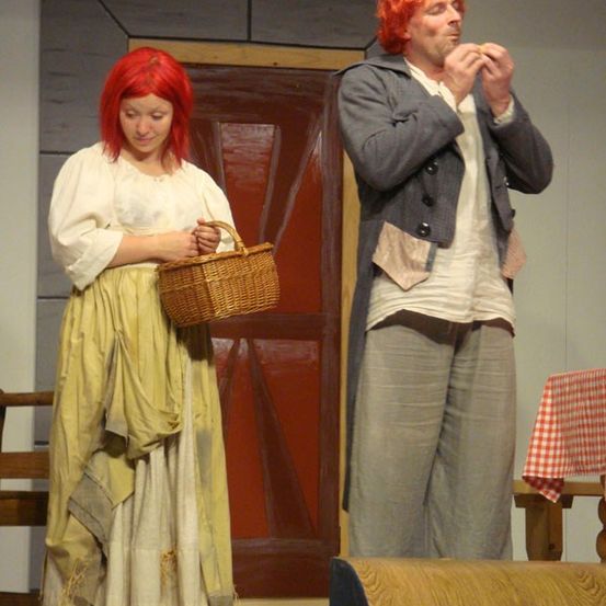 Ein Mann und eine Frau stehen auf der Bühne, die Frau hält einen Korb und der Mann isst etwas.