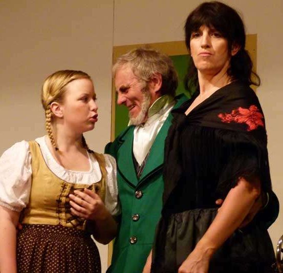 Drei Personen stehen in einem Raum zusammen, die Frau rechts scheint die anderen anzusprechen.