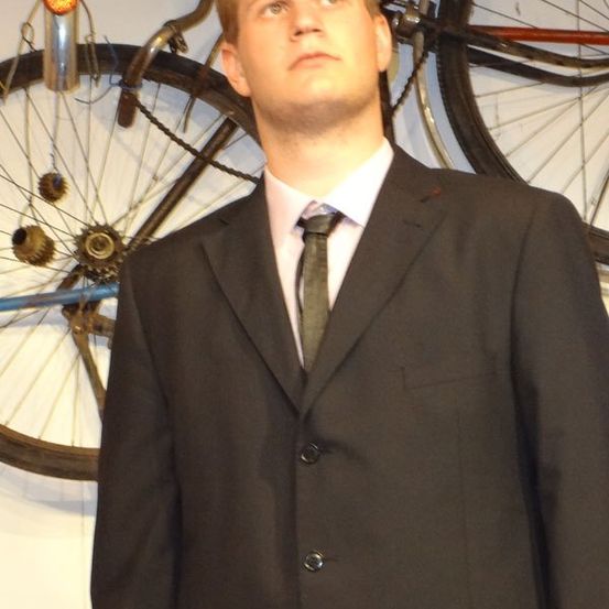 Ein Mann in einem schwarzen Anzug steht vor einer Wand mit aufgehängten Fahrradrädern.