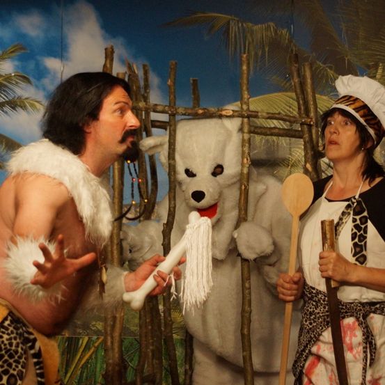 Ein Mann in einem Pelzkostüm und eine Frau in einer Kochmütze halten Requisiten. Dahinter steht eine Person in einem weißen Bärenkostüm.