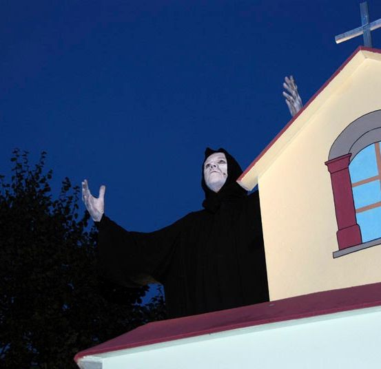 Eine Person in einer Geisterverkleidung steht bei Nacht auf dem Dach einer Kirche.