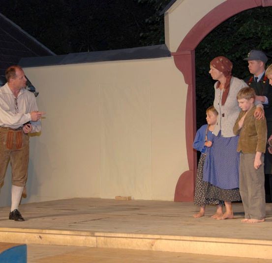 Eine Gruppe von Menschen steht nachts auf einer hölzernen Bühne, möglicherweise in Probe für ein Theaterstück.