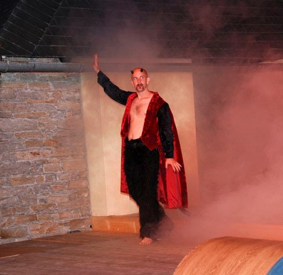 Ein Mann in einem roten Umhang und schwarzen Hosen winkt auf der Bühne mit einem Raucheffekt.