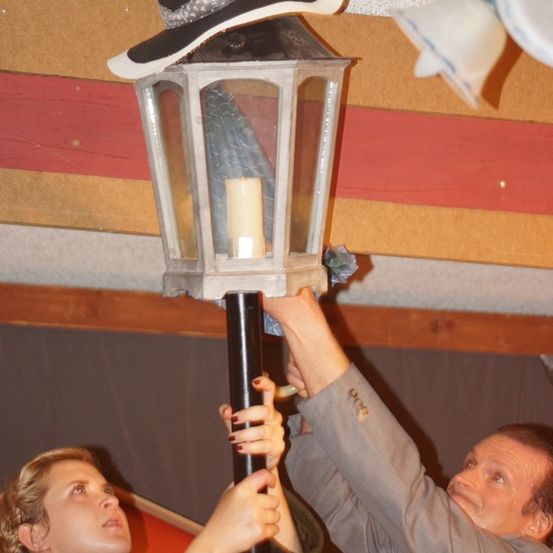 Ein Mann und eine Frau stellen eine Laterne auf einem Pfosten ein, mit einem Hut, der daran hängt.