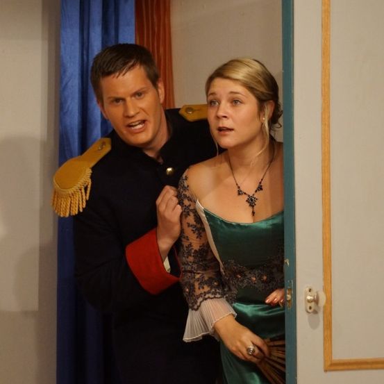 Ein Mann in Uniform steht neben einer Frau in einem smaragdgrünen Kleid, beide sehen den Betrachter an.