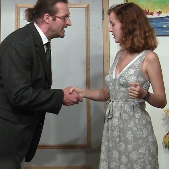 Ein Mann und eine Frau schütteln sich die Hände in einem Raum mit einer weißen Tür und einem Gemälde an der Wand.