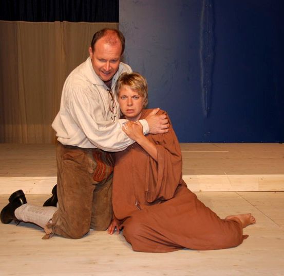 Ein Mann und eine Frau sind auf der Bühne, der Mann kniet und umarmt die Frau von hinten.