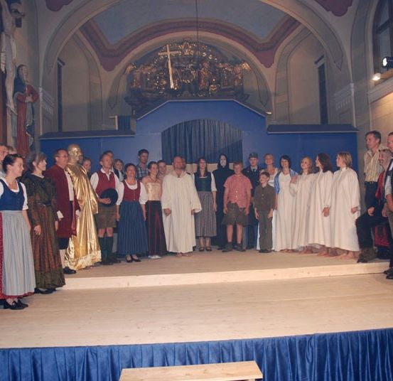 Eine Gruppe von Menschen in traditionellen Kostümen steht auf einer Bühne in einer Kirche.