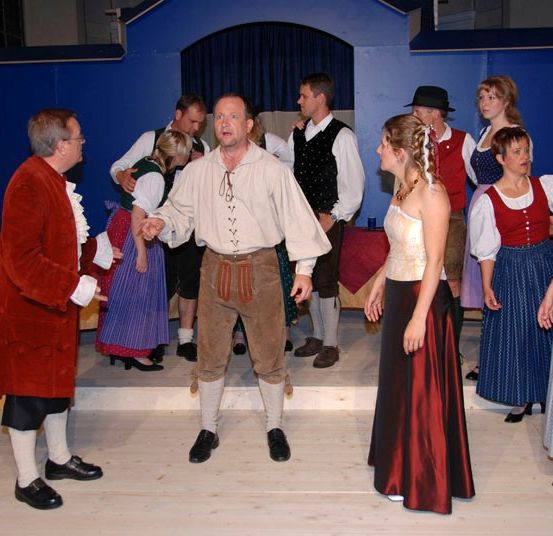 Eine Gruppe von Menschen in traditioneller Kleidung führt auf einer Bühne mit blauem Hintergrund auf.