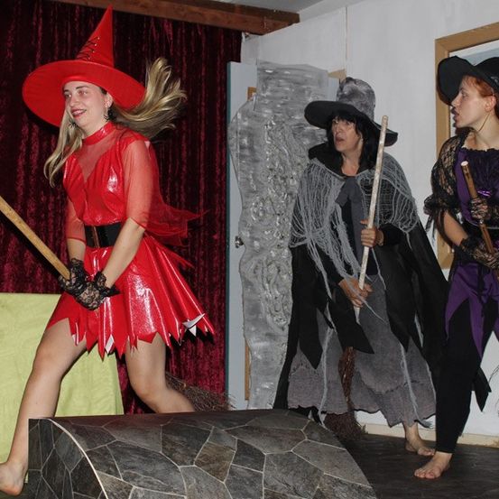 Drei als Hexen verkleidete Frauen führen auf der Bühne auf, eine in einem roten Kostüm in der Führung.
